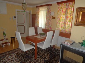 Un comedor con una mesa de madera, sillas blancas, un tapete estampado y un radiador.