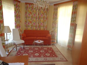 A living room with a sofa, a chair, a coffee table, a chandelier, and floral curtains.