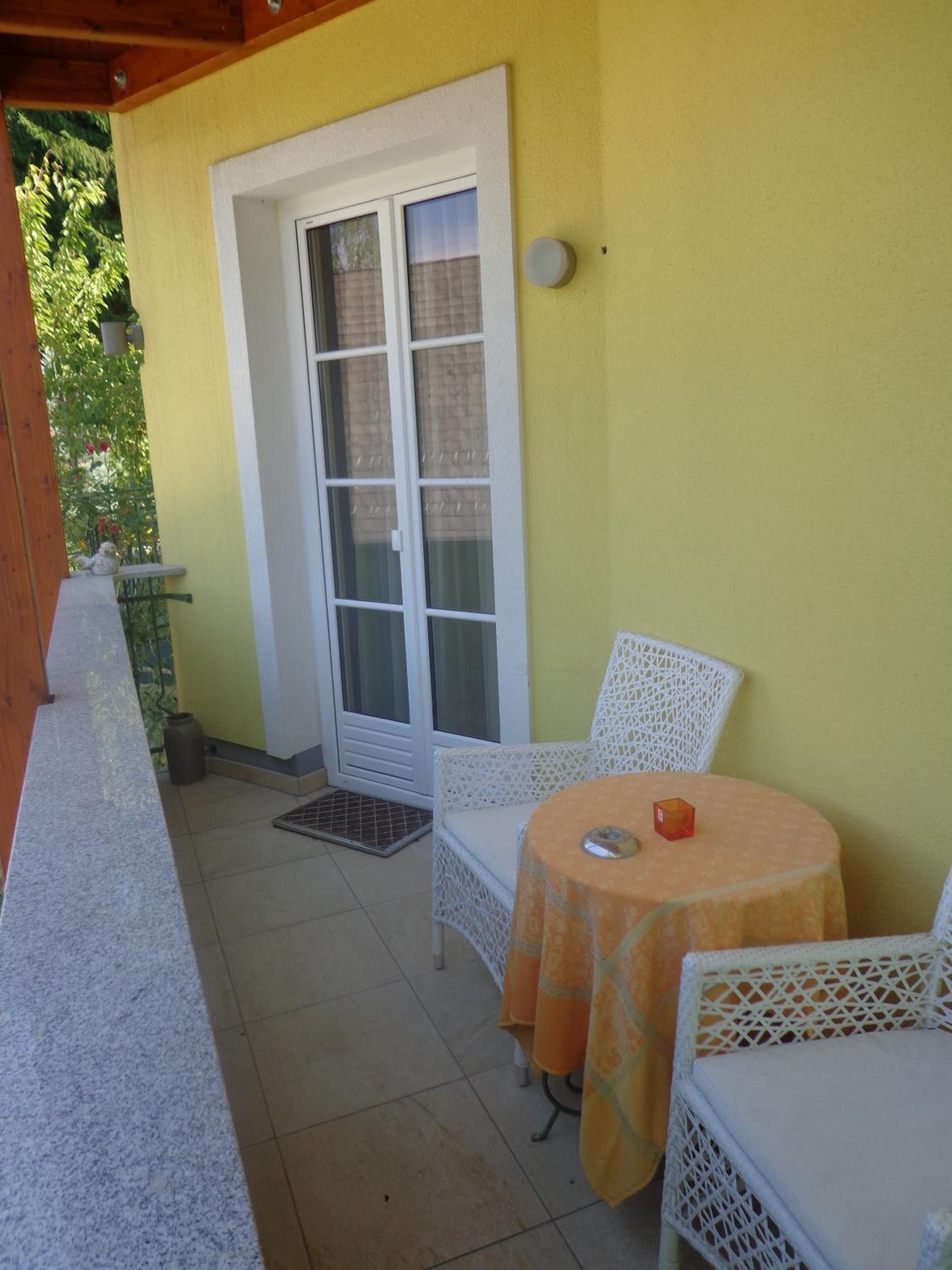 A covered patio with a white chair and a small table, a sliding glass door, and a yellow wall.