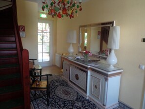 A room with a wooden staircase, a large mirror, a white console table with a vase of flowers, and a patterned rug.
