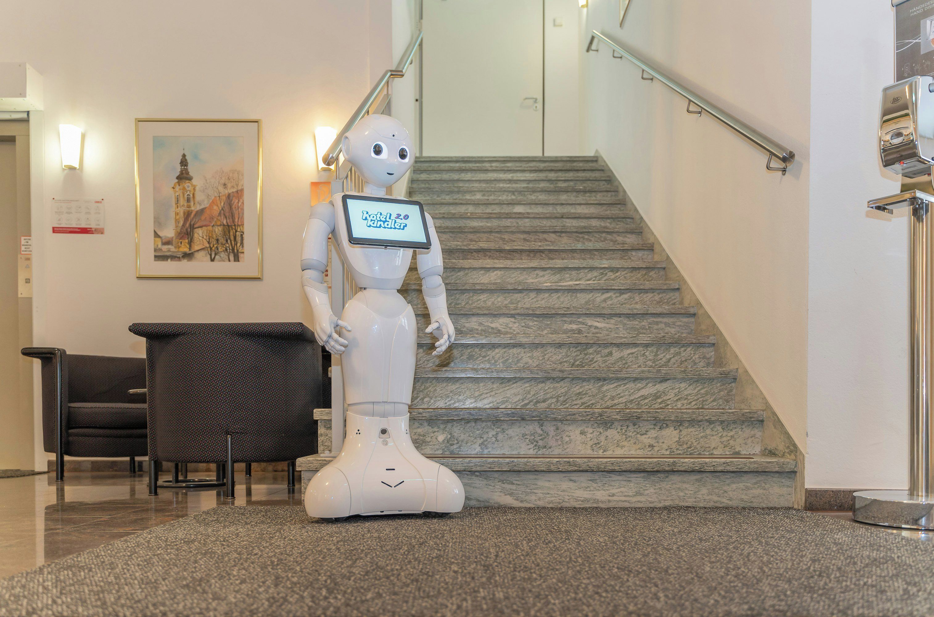 Un robot con una pantalla en un vestíbulo con una escalera y un cuadro en la pared.
