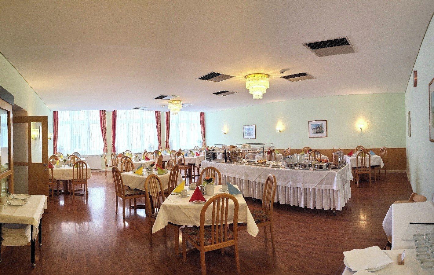 Un amplio comedor con varias mesas y sillas, ventiladores de techo e iluminación en las paredes.