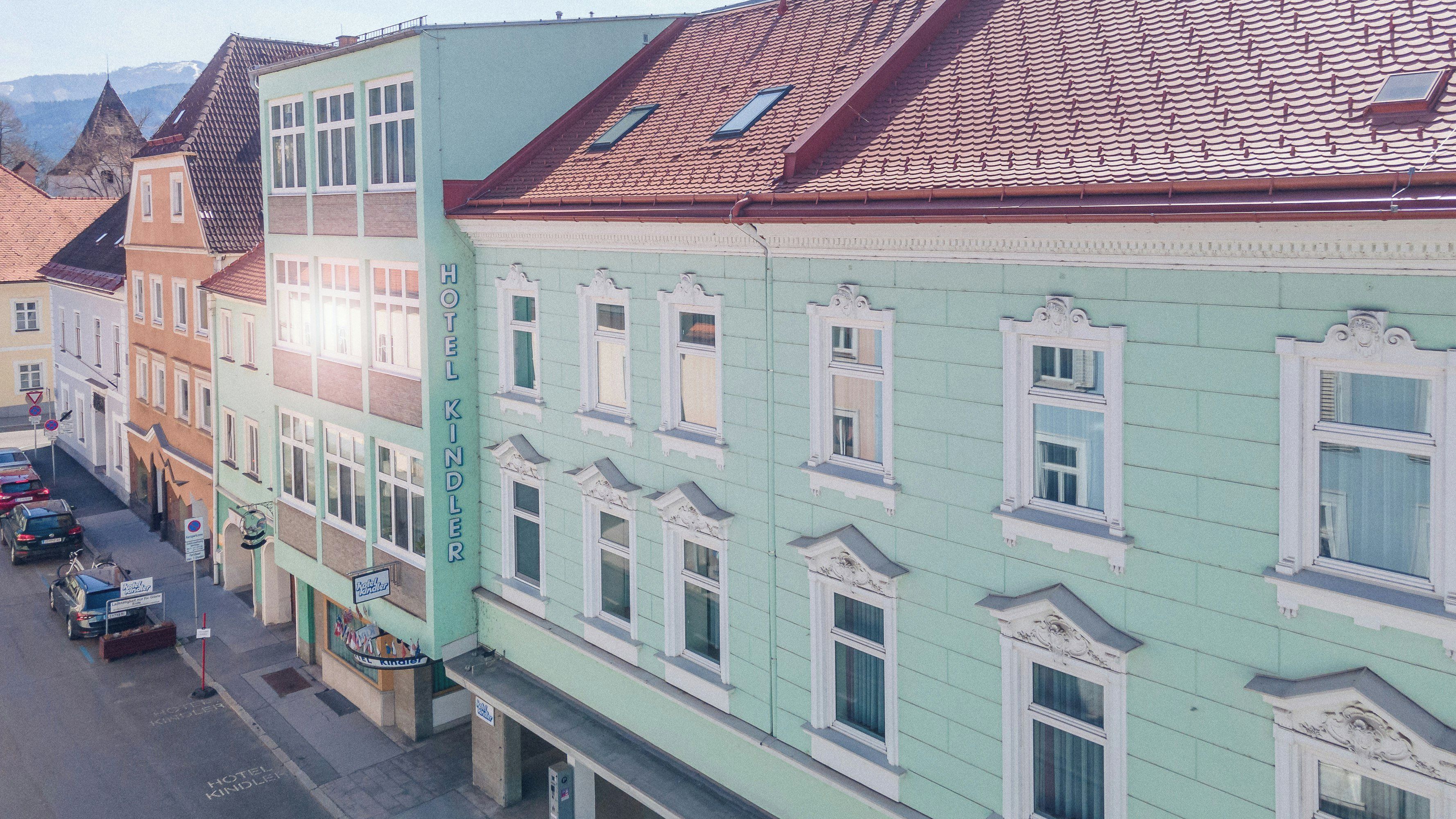 Ein mehrstöckiges Gebäude mit grüner Fassade, zahlreichen Fenstern und einem Schild, das es als Hotel kennzeichnet.