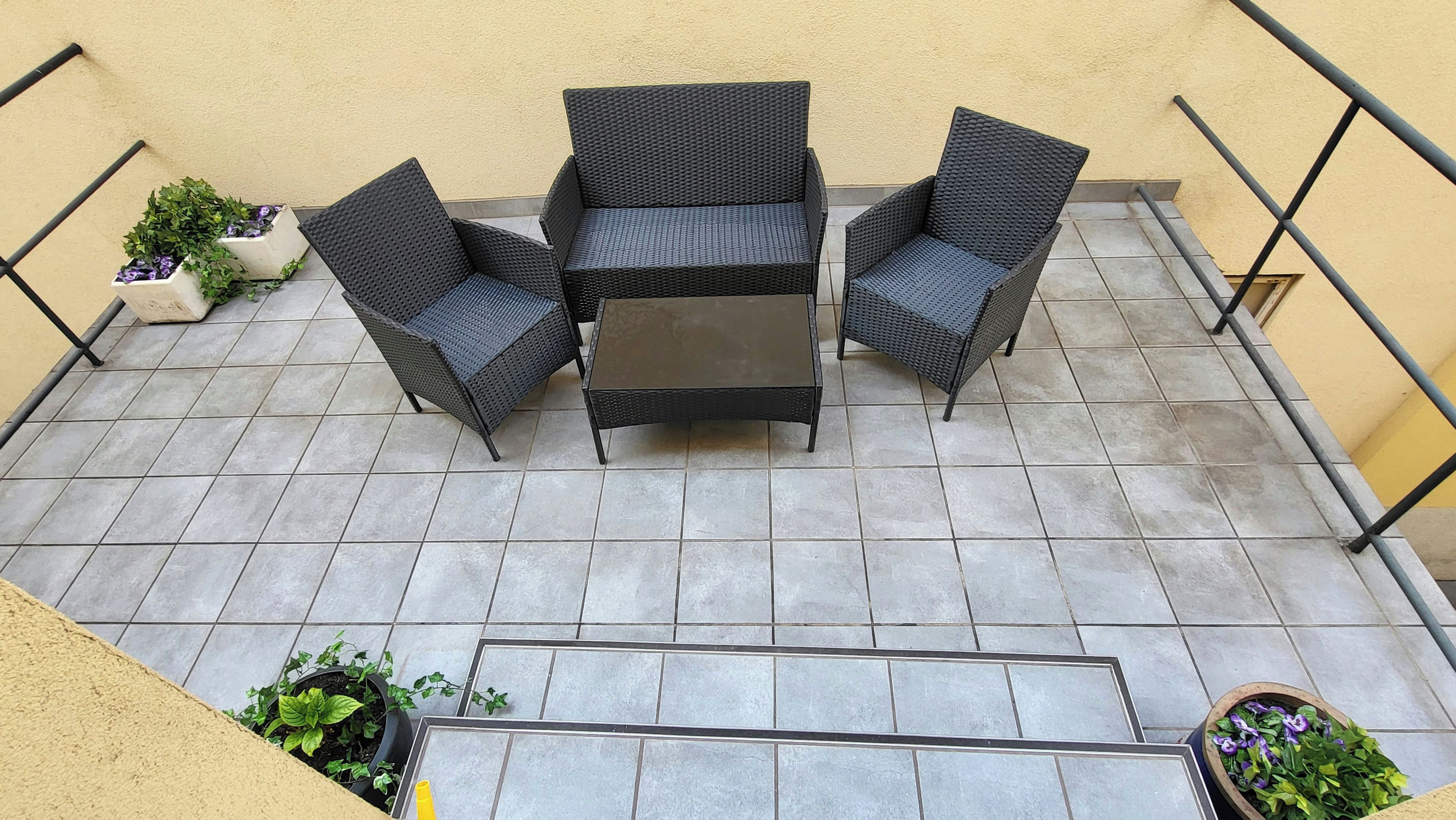 Un balcón con una mesa y sillas, rodeado de plantas en macetas.