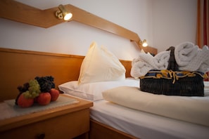 A hotel room with a neatly made bed, a bedside table with fruit, and a basket of towels.