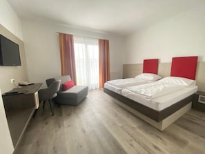 A hotel room with a bed, a desk, a chair, and a television mounted on the wall.
