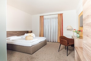 A hotel room with a bed, a desk, a chair, a lamp, and a window with curtains.
