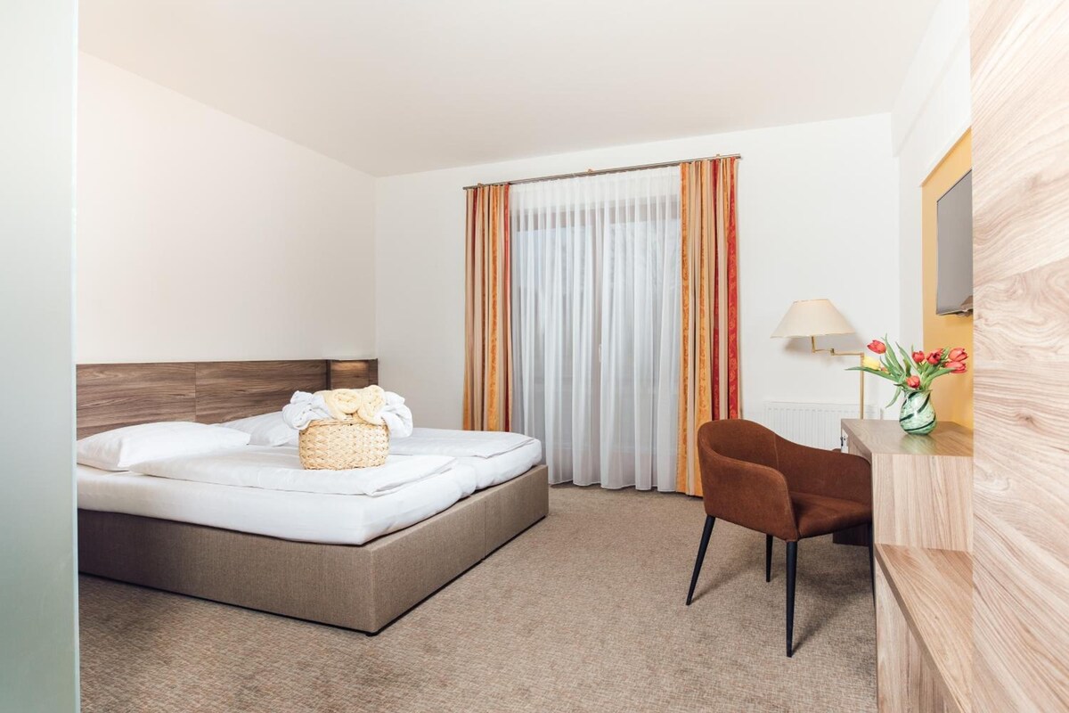 A hotel room with a bed, a desk, a chair, a lamp, and a window with curtains.