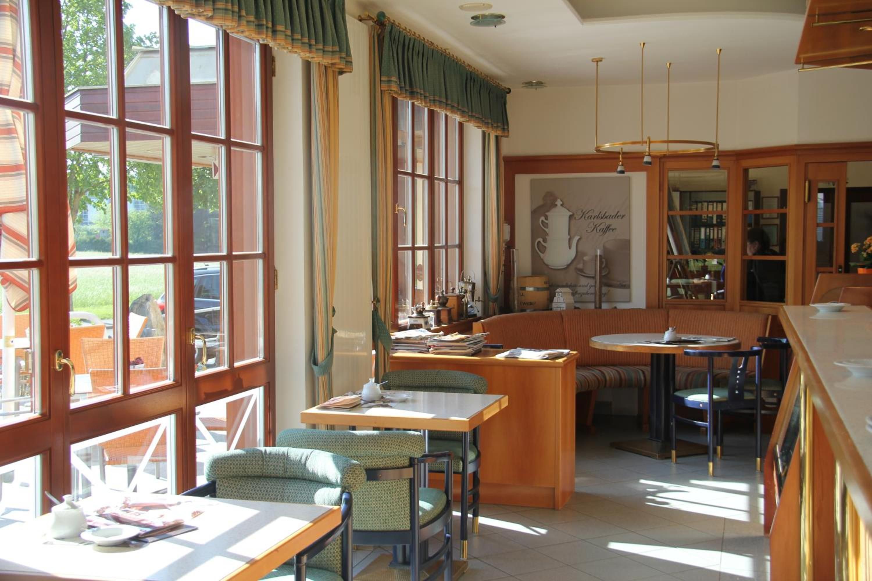 Una cafetería acogedora con amplias ventanas, una zona central de mesas y una barra de servicio.