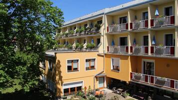 Un hotel de varios pisos con balcones, una zona de estar al aire libre techada y un jardín cuidado.