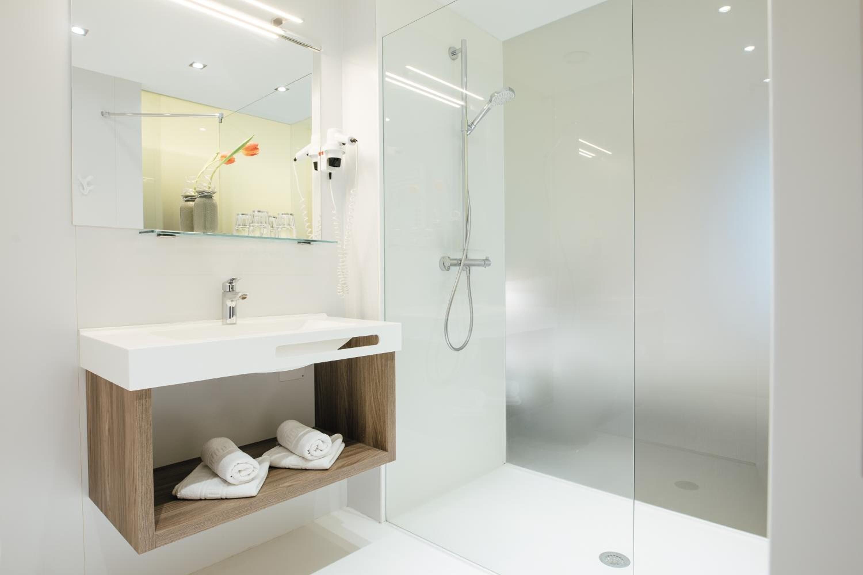 Un baño moderno con cabina de ducha de vidrio, un lavabo blanco y un mueble de tocador de madera con toallas.