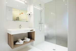 A modern bathroom with a glass shower enclosure, a white sink, and a wooden vanity with towels.