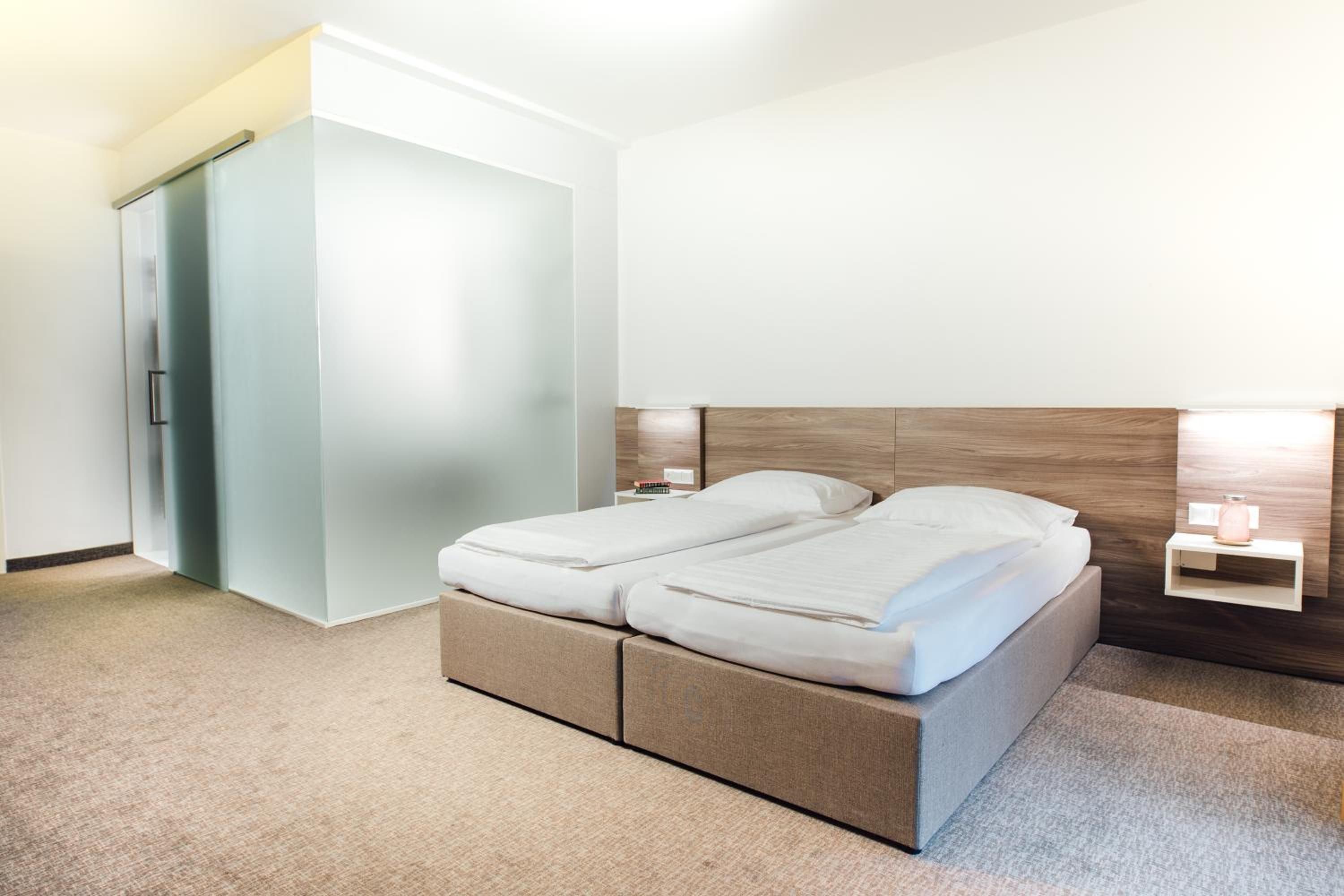 Una habitación de hotel con una cama, un armario y una mesita de noche con lámpara.