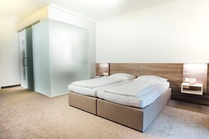Una habitación de hotel con una cama, un armario y una mesita de noche con lámpara.