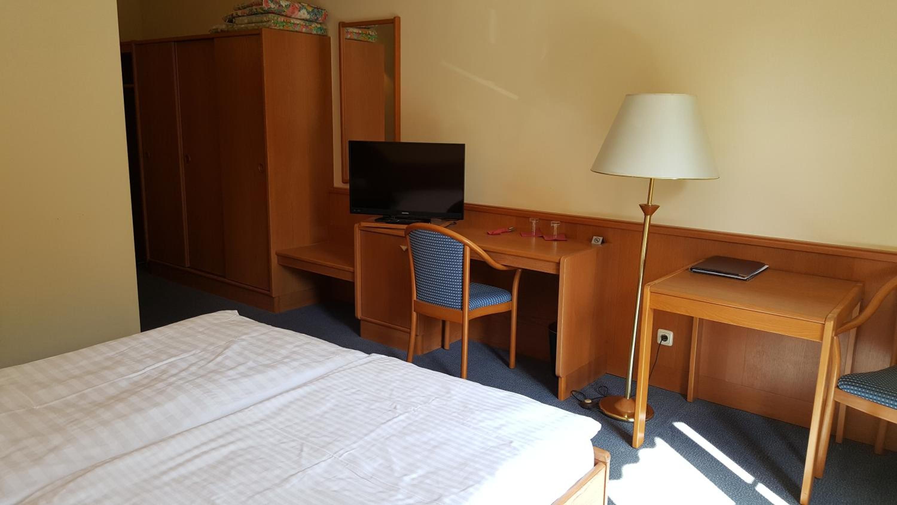 Ein Hotelzimmer mit Bett, Schreibtisch, Stuhl, Fernseher und Lampe.