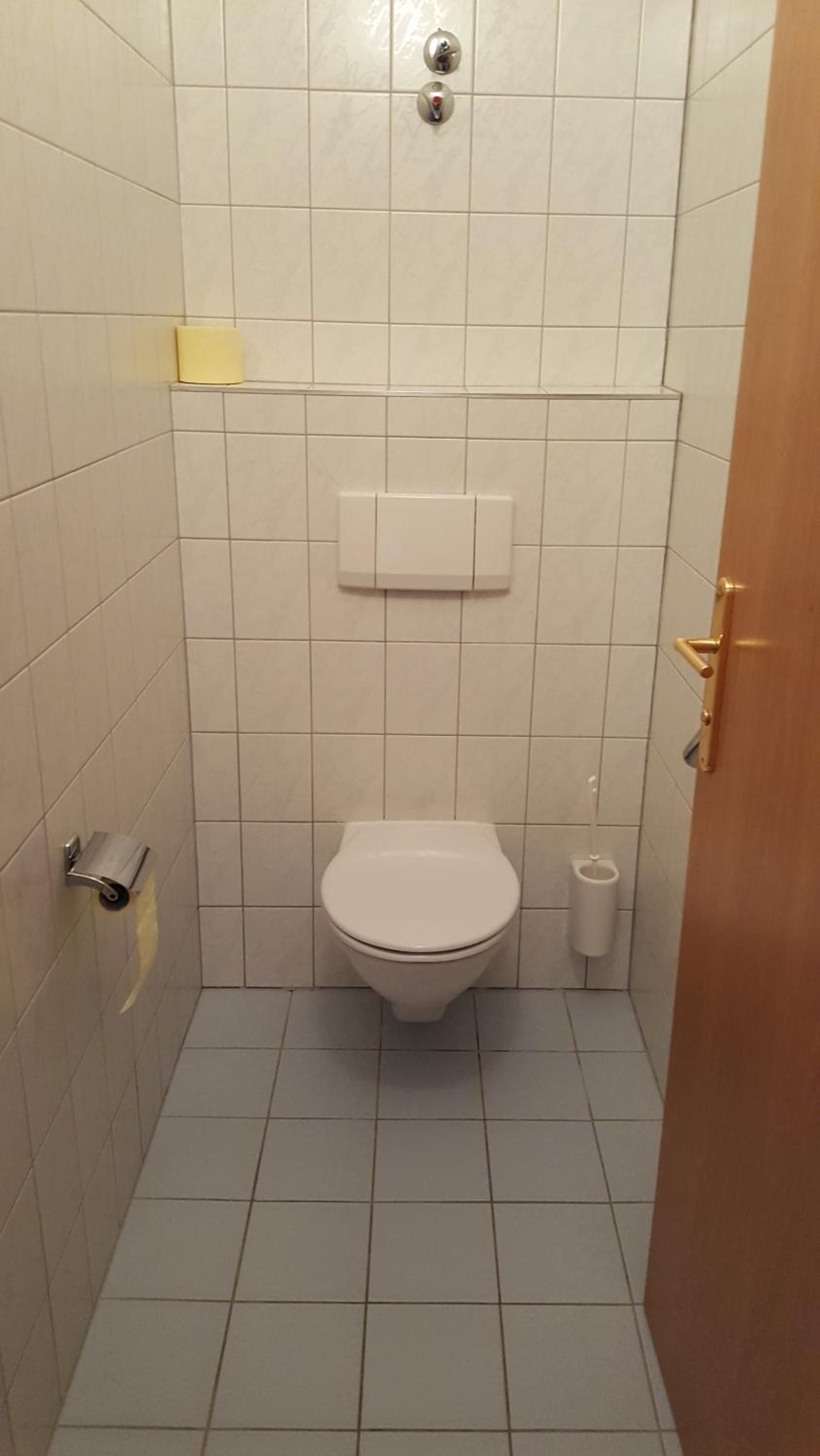 Ein kleines Badezimmer mit Fliesen, einer Toilette, einem Händetrockner und einem Papiertuchspender.