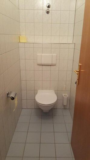 A small, tiled bathroom with a toilet, a hand dryer, and a paper towel dispenser.