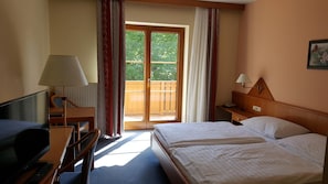 A hotel room with a bed, a desk with a lamp, a television, and a view of the outside.