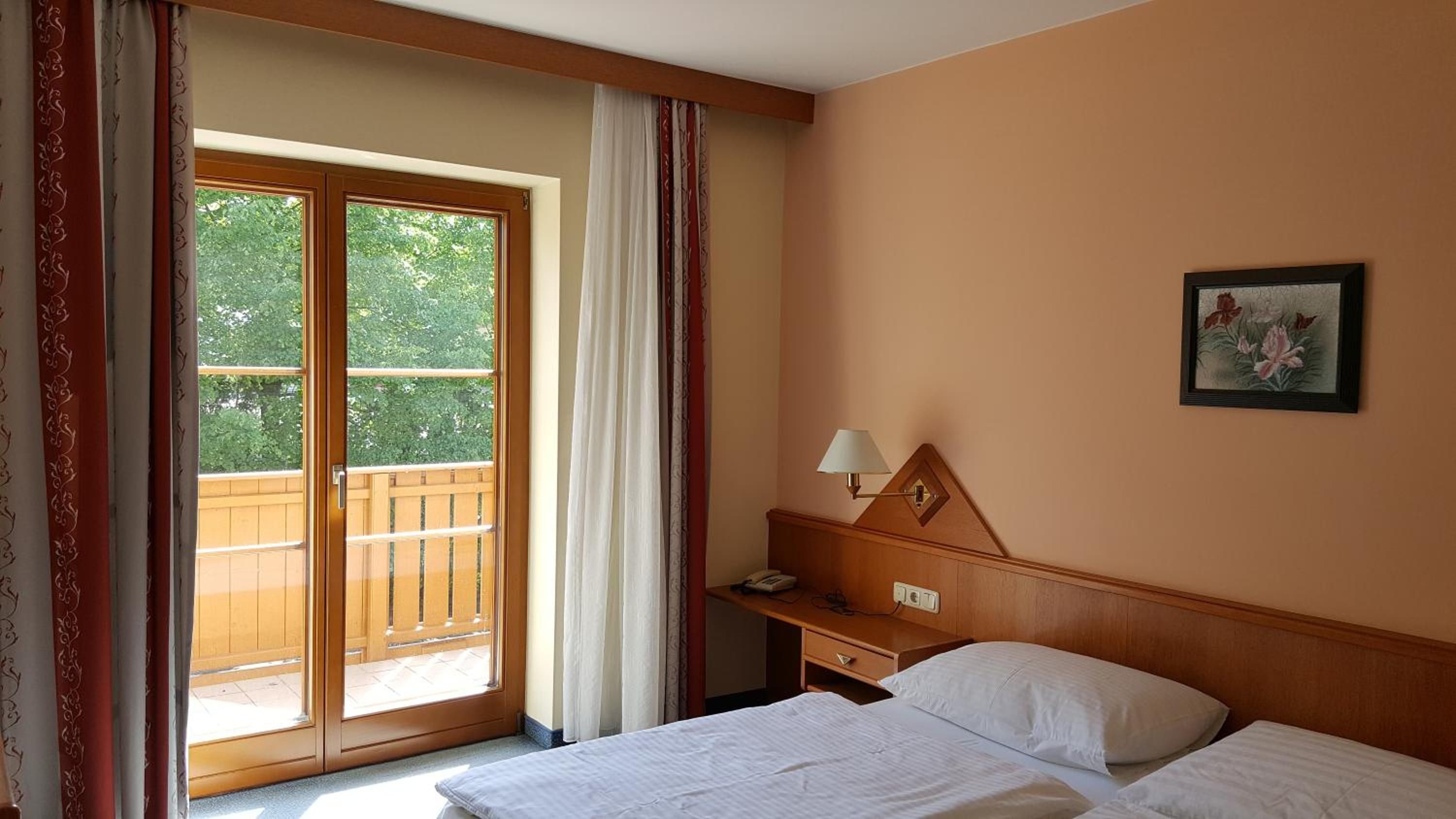 Ein Hotelzimmer mit Bett, Nachttisch, Lampe, einem Gemälde und einer Glastür zum Balkon.
