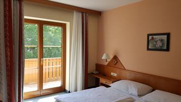 Ein Hotelzimmer mit Bett, Nachttisch, Lampe, einem Gemälde und einer Glastür zum Balkon.