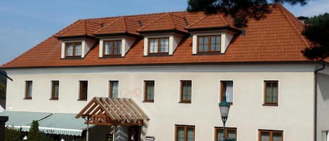 A two-story building with a red-tiled roof, multiple windows, and a small entrance pavilion.