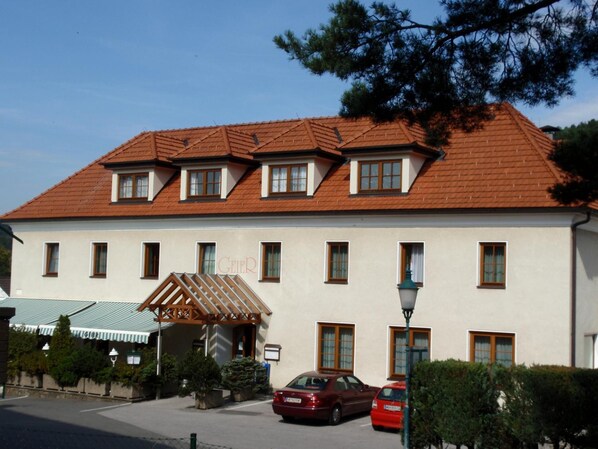 A two-story building with a red-tiled roof, multiple windows, and a small entrance pavilion.