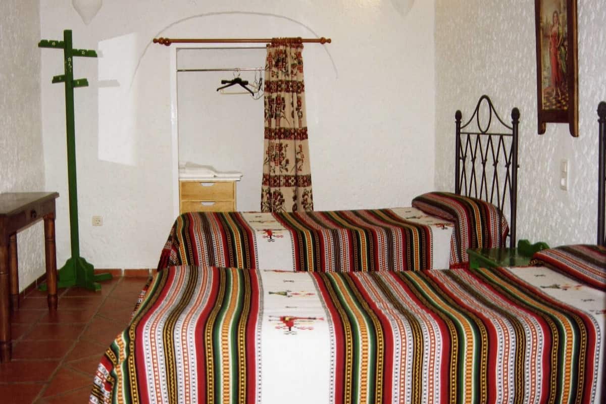 Een kamer met twee bedden, een houten tafel, een groene stoel, een spiegel en een deur met gordijn.