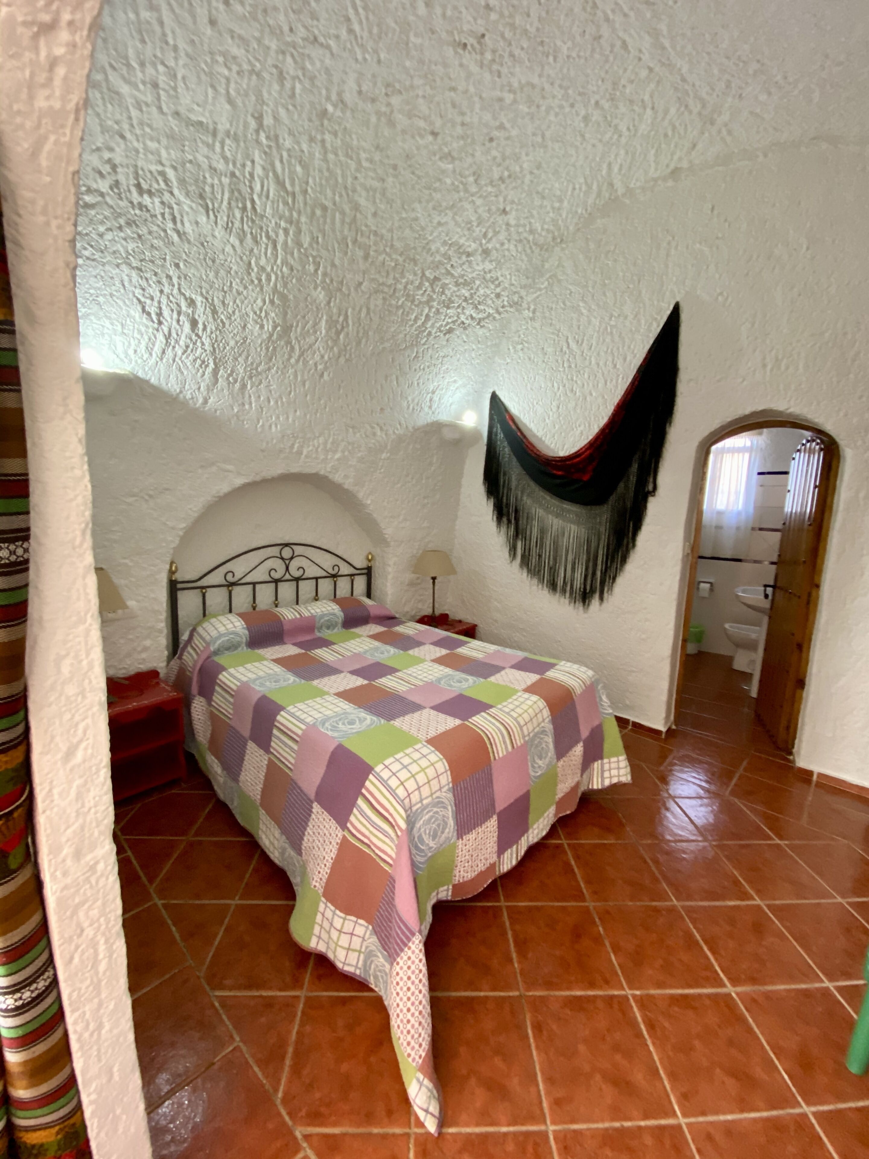 Une chambre à coucher avec un lit, un fauteuil suspendu et une salle de bain visible à travers une arche.