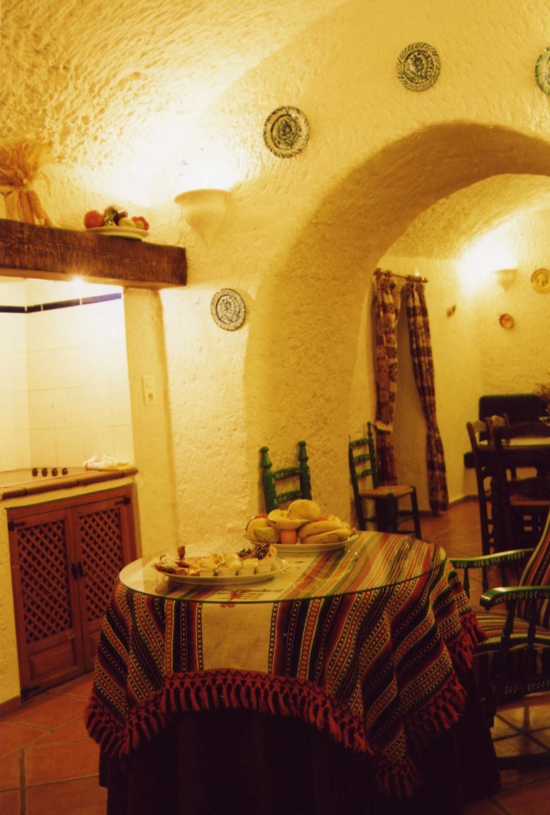 Ein Essbereich mit einem runden Tisch, der mit einer gemusterten Tischdecke bedeckt ist und von Stühlen umgeben wird.