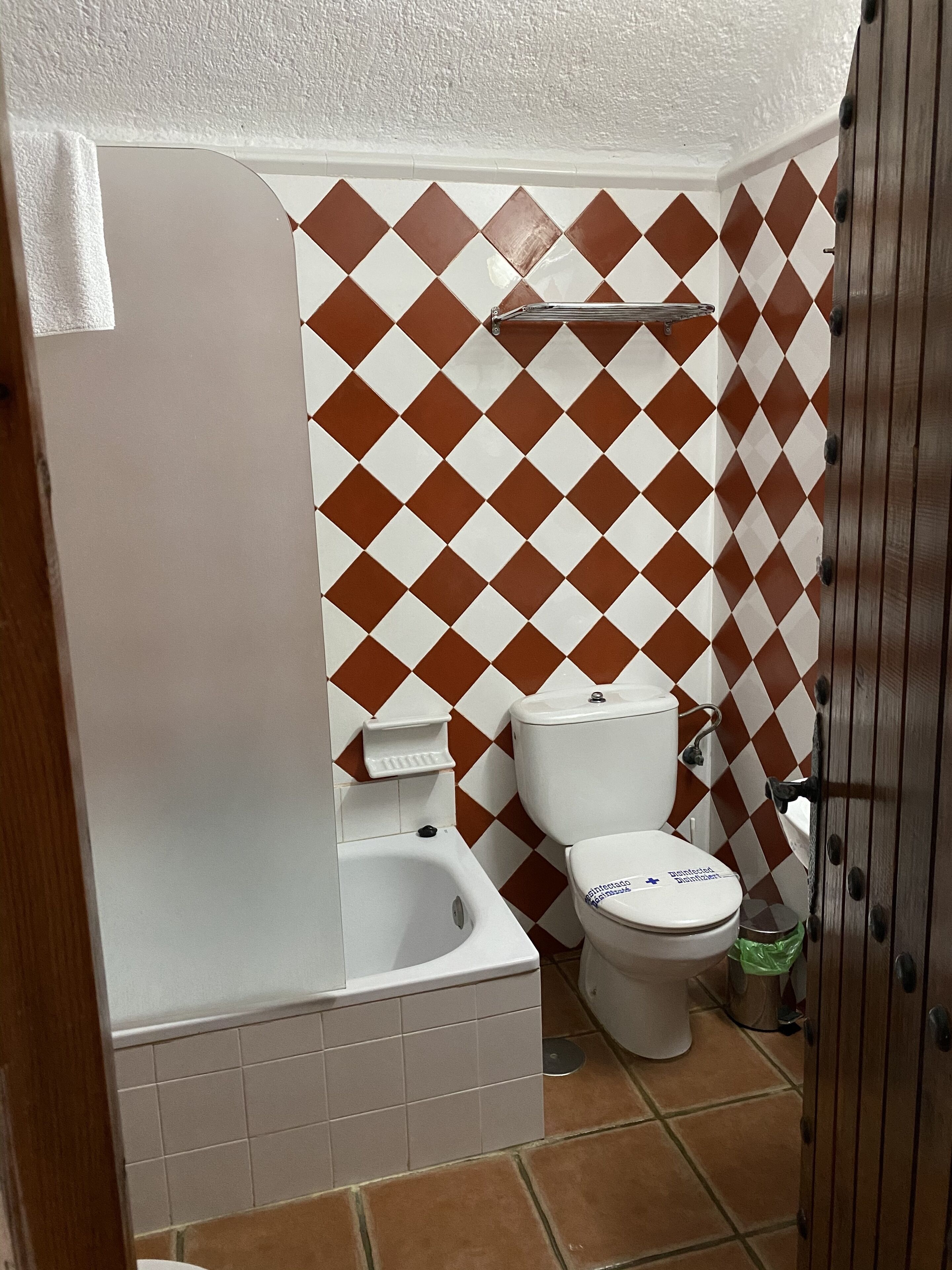 Un baño con una bañera blanca, un inodoro blanco y un bidé. Las paredes presentan un estampado a cuadros marrones y blancos.