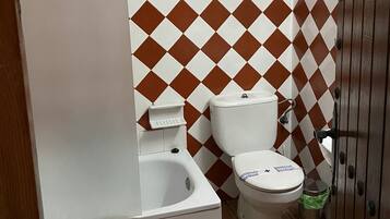 Un baño con una bañera blanca, un inodoro blanco y un bidé. Las paredes presentan un estampado a cuadros marrones y blancos.