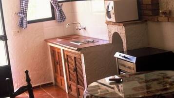 Cocina pequeña con ventana, microondas, lavabo y una mesa con una silla.
