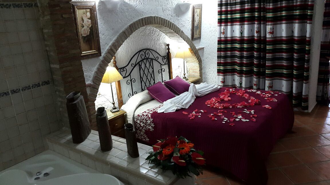 A bedroom with a bed, a nightstand, a lamp, a vase with flowers, and a bathtub.