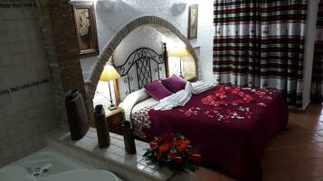 A bedroom with a bed, a nightstand, a lamp, a vase with flowers, and a bathtub.