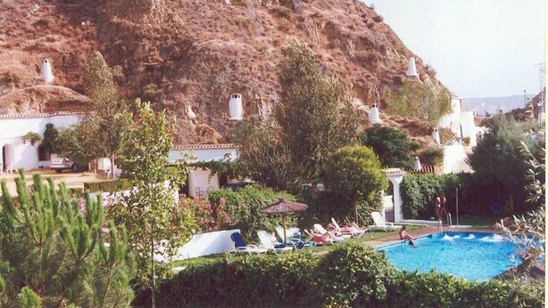 Een zwembad met ligbedden en een berg op de achtergrond.