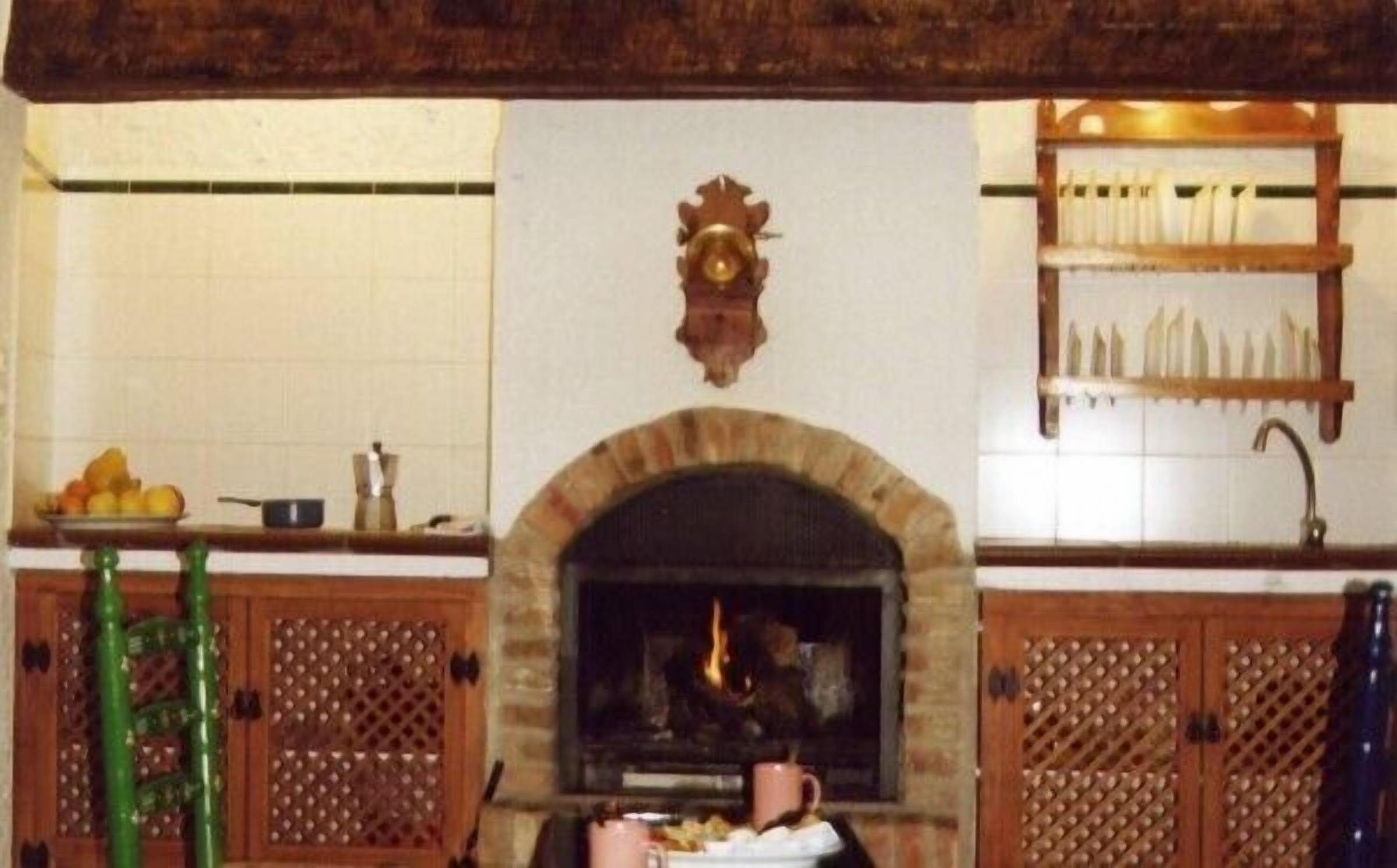 A kitchen with a stone fireplace, wooden cabinets, and a fruit bowl on the counter.