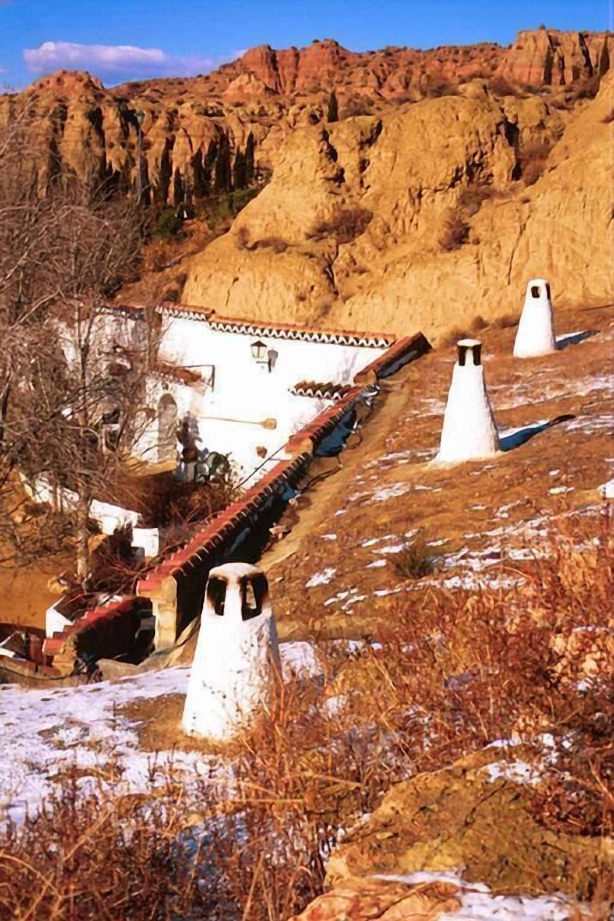 A traditional building with a sloped roof, surrounded by rocky terrain and sparse vegetation.