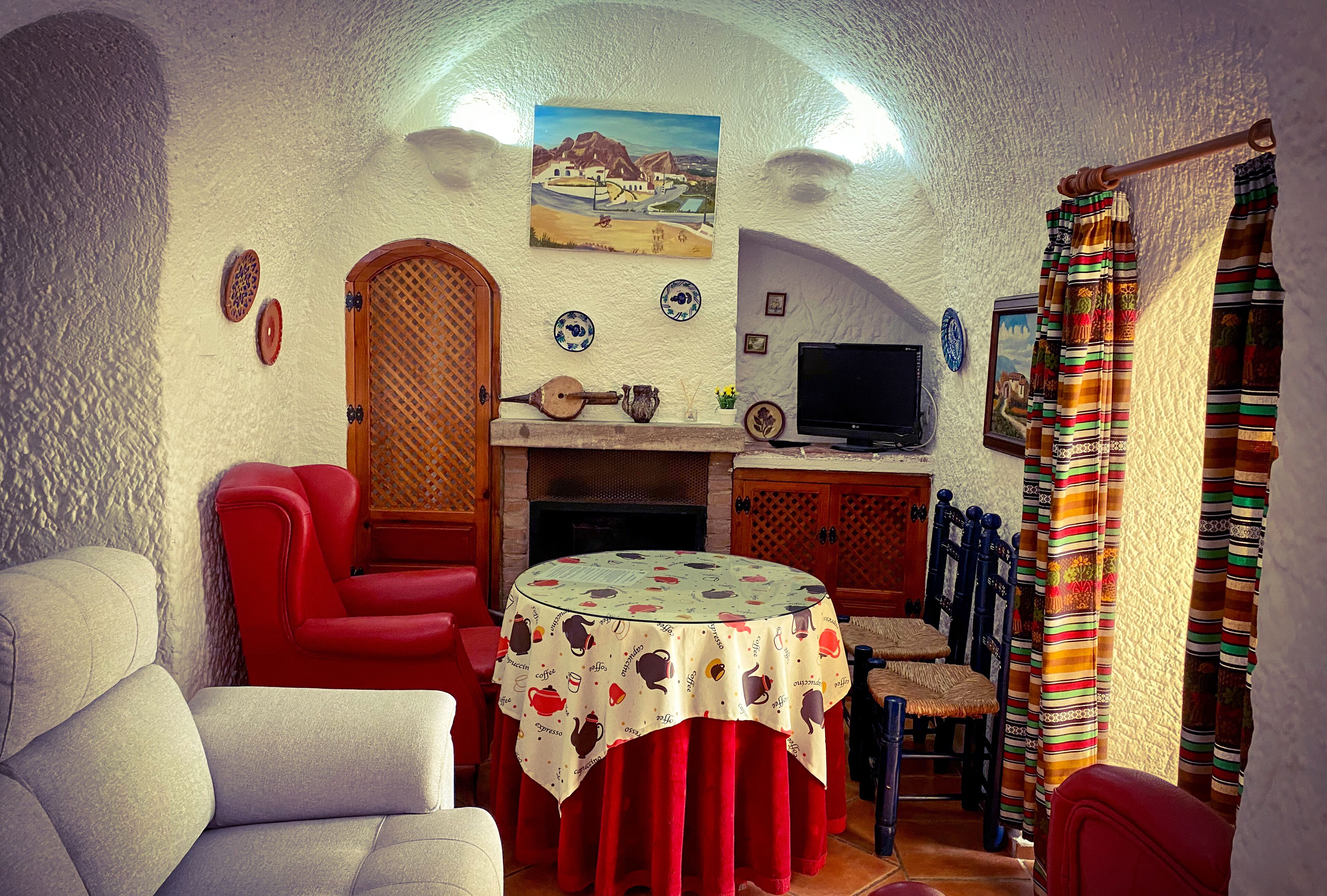 Ein gemütliches Wohnzimmer mit Kamin, einem runden Tisch mit Tischdecke, roten Sesseln und einem Fernseher.
