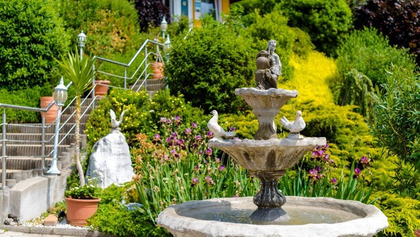 A garden with a fountain, potted plants, and a building in the background. - 1a Hotel Steiner (Judenburg)