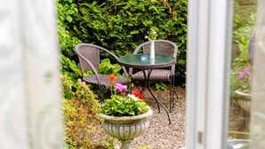 An outdoor seating area with wicker chairs and a glass table, surrounded by greenery and a decorative urn. - 1a Hotel Steiner (Judenburg)