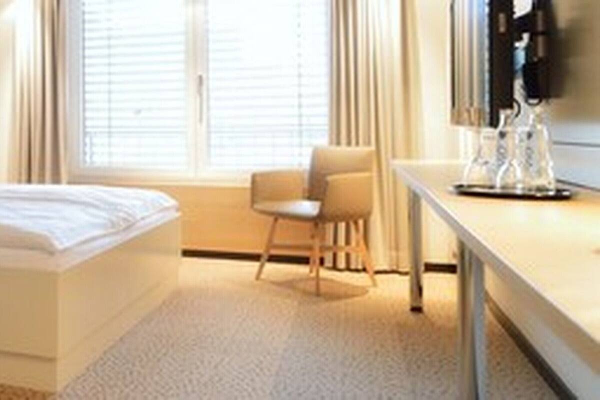 A hotel room with a bed, a desk, a chair, and a window with blinds.