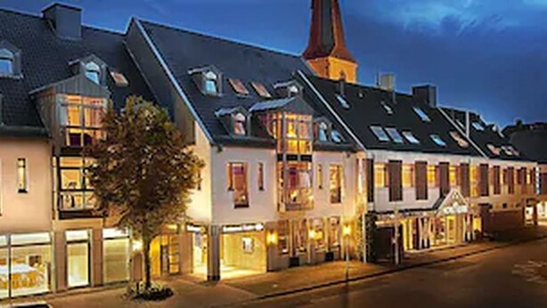 A row of traditional European-style buildings with multiple stories, large windows, and a prominent church steeple. - Hotel Restaurant Reuter (Rheda-Wiedenbruck)
