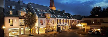 Una hilera de edificios tradicionales de estilo europeo, con varios pisos, ventanas amplias y una imponente aguja de iglesia.