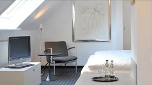 A hotel room with a bed, a desk with a computer, a chair, and a small table with bottles. - Hotel Restaurant Reuter (Rheda-Wiedenbruck)