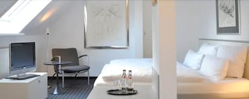 Habitación de hotel con una cama, un escritorio con computadora, una silla y una mesita con botellas.