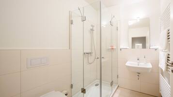 A modern bathroom with a glass-enclosed shower, a white sink, and a toilet.