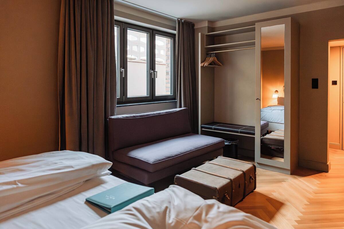 A hotel room with a bed, a seating area, a wardrobe, and a mirror.