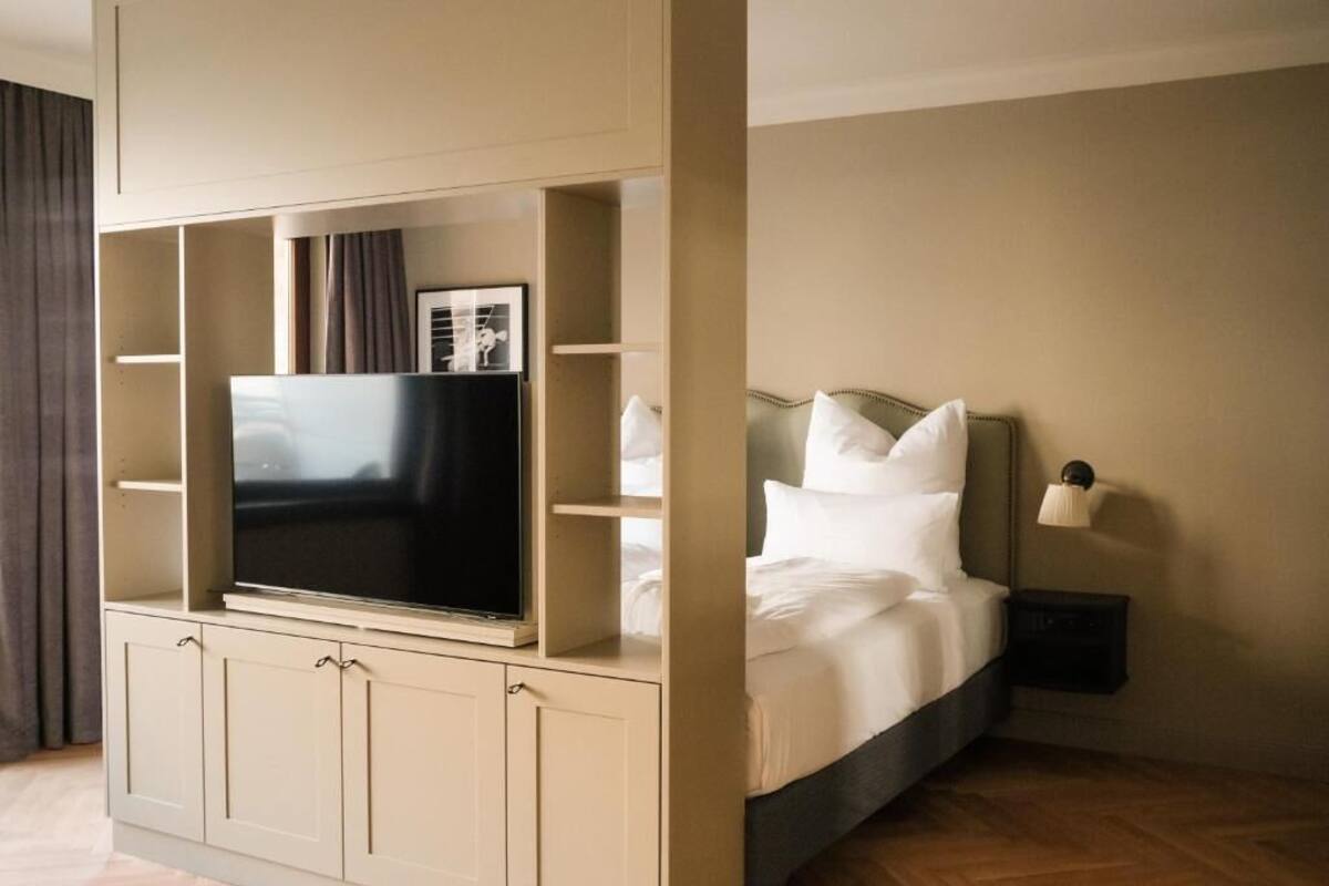 A hotel room with a bed, a TV mounted on a cabinet, a nightstand, and a wall-mounted lamp.