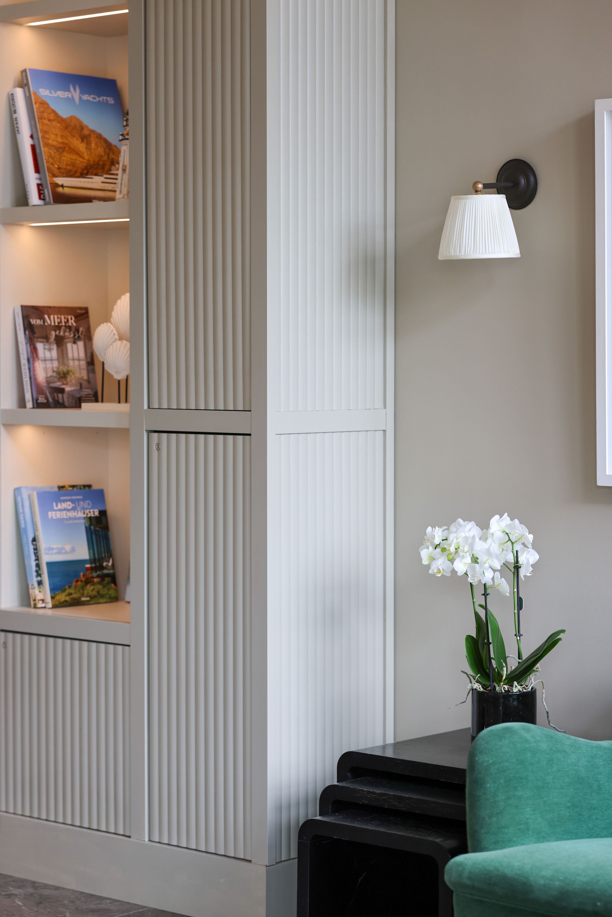 A modern interior with a bookshelf, a wall-mounted lamp, and a potted orchid.