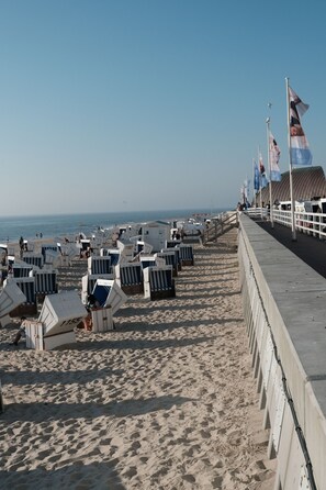A beachside promenade with rows of beach chairs and umbrellas, a concrete walkway, and flags. - Mimosa Hotel (Sylt)